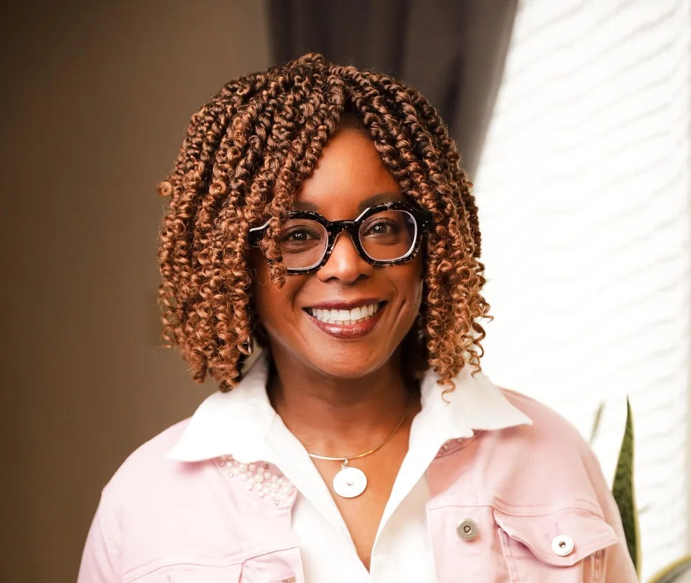 Dr Helen Ofosu, Coach, Consultant, Speaker, and Author, smiling, wearing a white blouse and pink jean jacket