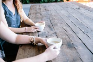 Two ladies sitting at a table with a coffee cup discussing a death