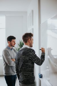 two guys near whiteboard discuss blockchain technology